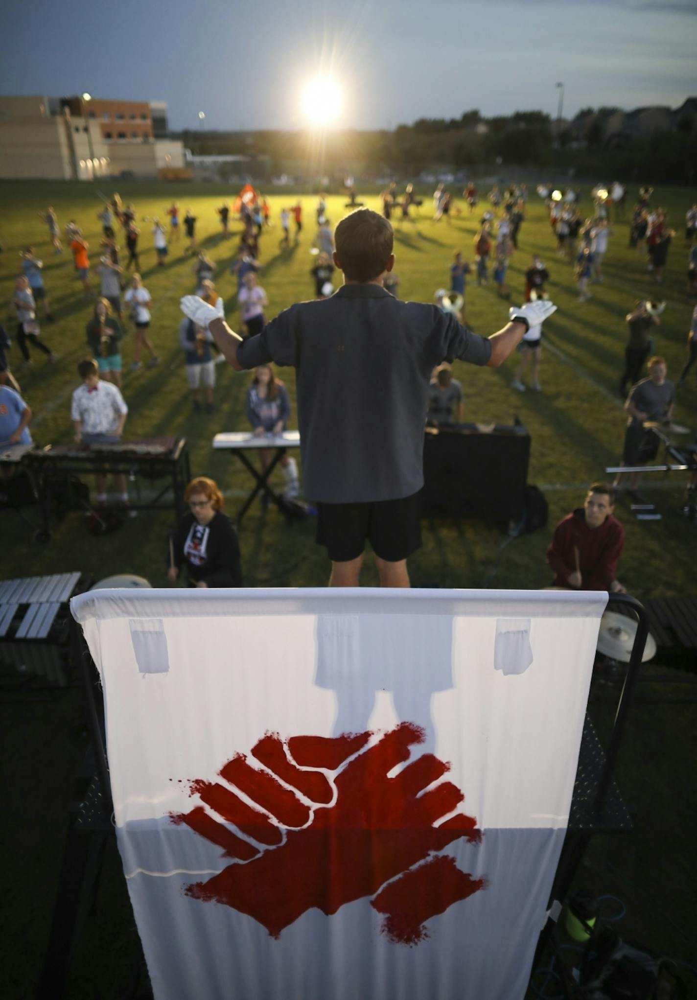 Drum major Noah Budde conducted the Farmington High School marching band during rehearsal of their program "Dystopia." A revised banner with hands clasped hangs from the platform he stood on.