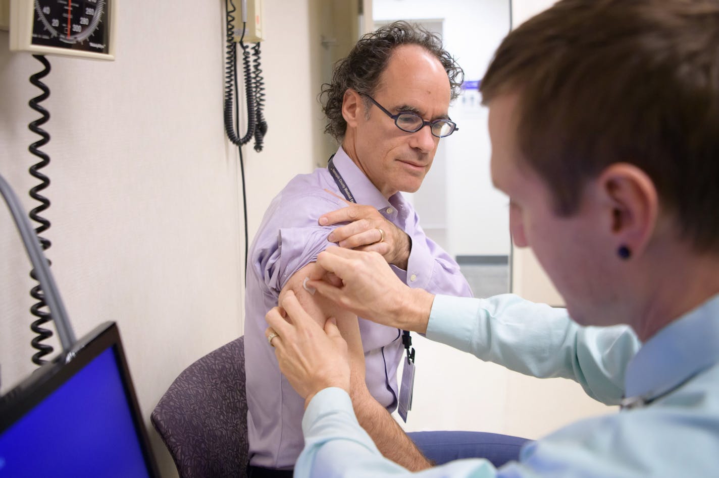 HCMC chief cardiologist Dr. Bradley Bart prepped to get a flu shot from Josh Gramling, head of employee occupational health.