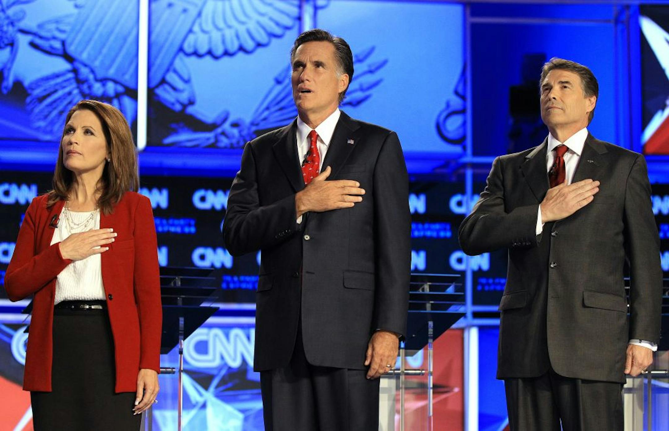 Republican presidential candidates, from left, Rep. Michele Bachmann, R-Minn, former Massachusetts Gov. Mitt Romney and Texas Gov. Rick Perry cover their hearts during the playing of the National Anthem before a Republican presidential debate Monday, Sept. 12, 2011, in Tampa, Fla.