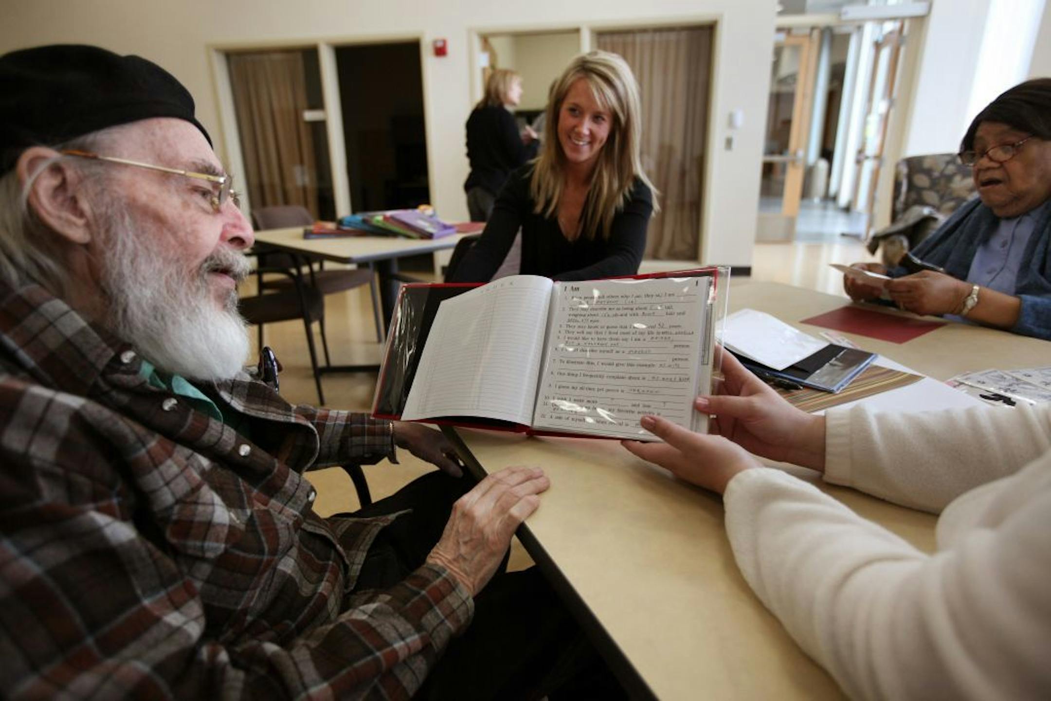 A new senior citizen campus, Heritage Park Senior Services Center, operated by Minneapolis Public Housing, includes new senior citizens center, a memory residence, and Senior YMCA. (IN THIS PHOTO) Bob Mathews (left) reads over his personal journal he created on his first day at the Augustana Open Circle day center program at Heritage Park. Program Coordinator Abbey Driscol (center) works with Leora Harris (right) on her journal. Gail Skoglund (right out of frame) is Director of Adult Day Service