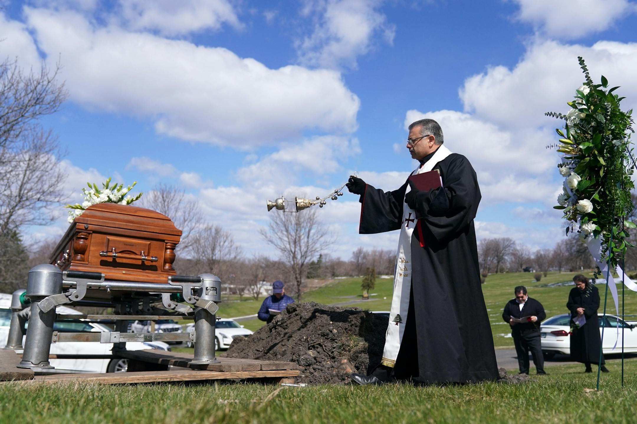 Chorbishop Sharbel Maroun, center, spread incense over the casket of Elie Farhat, who recently died of COVID-19 at the age of 92, as friends and family worked to keep the recommended distance from one another at his gravesite Thursday.
