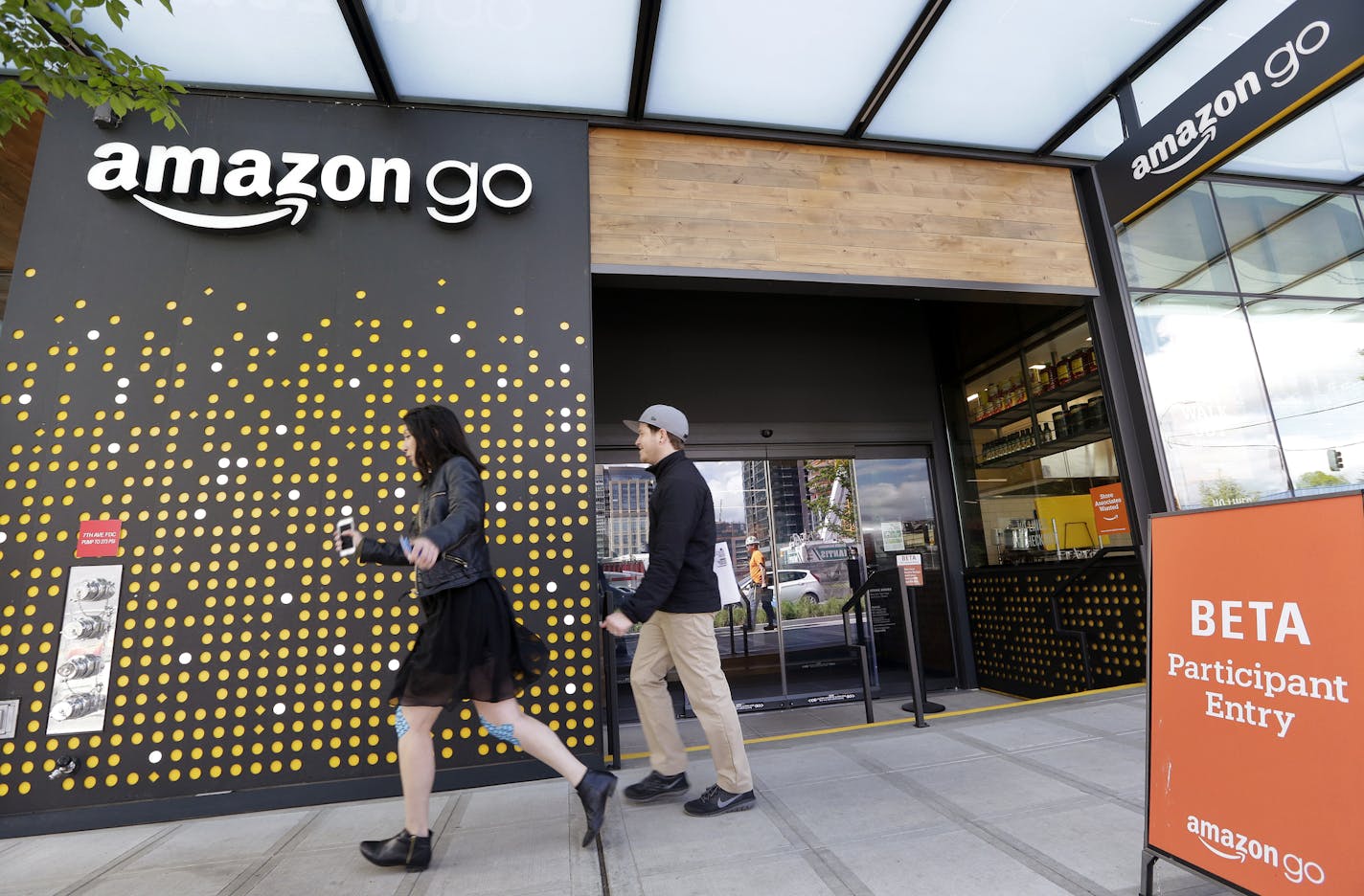 FILE - In this Thursday, April 27, 2017, file photo, people walk past an Amazon Go store, currently open only to Amazon employees, in Seattle. Amazon Go shops are convenience stores that don't use cashiers or checkout lines, but use a tracking system that of sensors, algorithms, and cameras to determine what a customer has bought. Wal-Mart&#x2019;s acquisition of Jet.com is accelerating its progress in e-commerce as it works to narrow the gap between itself and online leader Amazon. Wal-Mart is