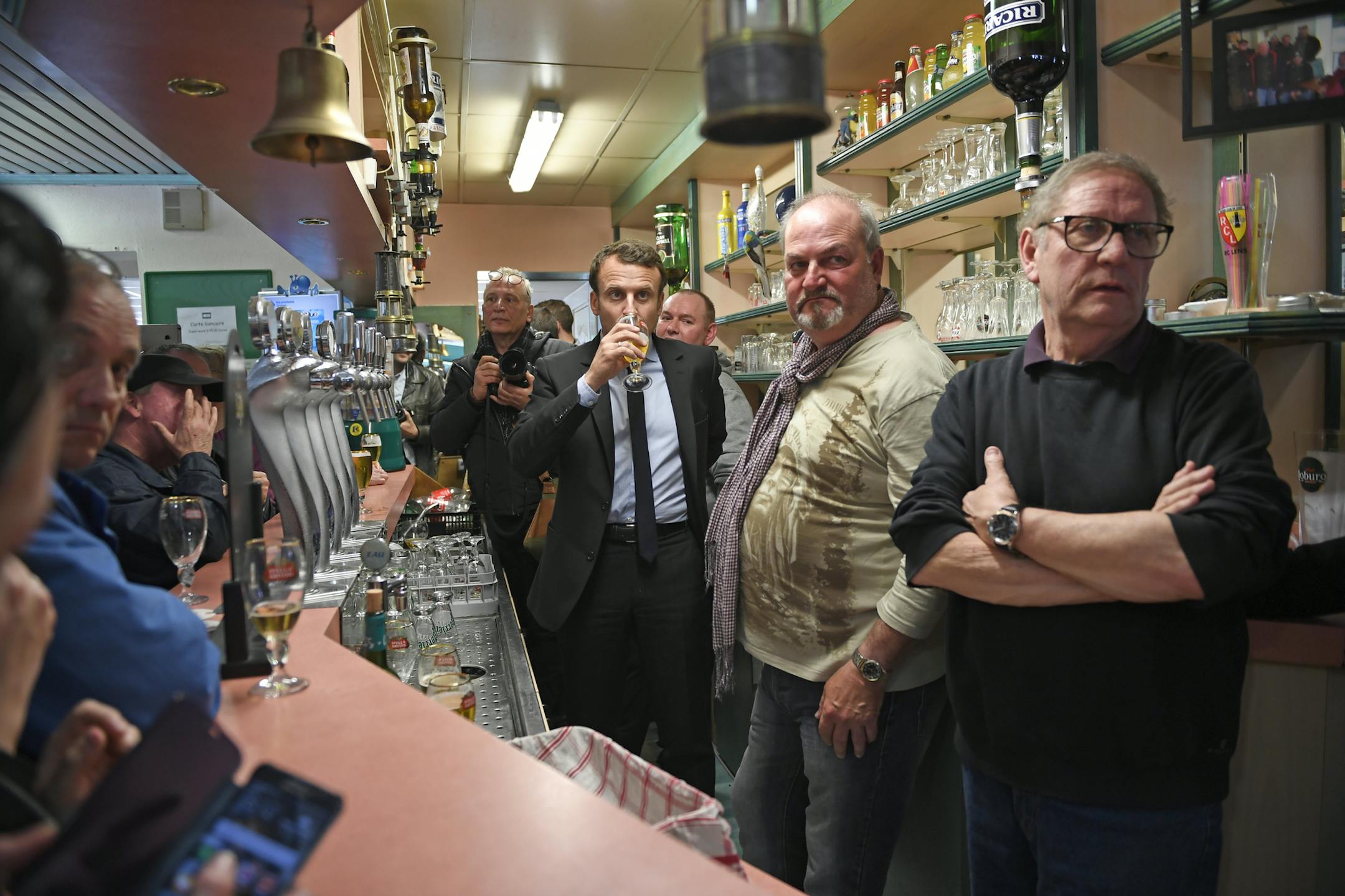 French centrist presidential election candidate Emmanuel Macron drinks a glass of beer as he speaks behind the bar counter, next to cafe owner Marc Piton, right, in a cafe in Bully-les-Mines, northern France, Wednesday, April 26, 2017 . (Eric Feferberg, Pool via AP)