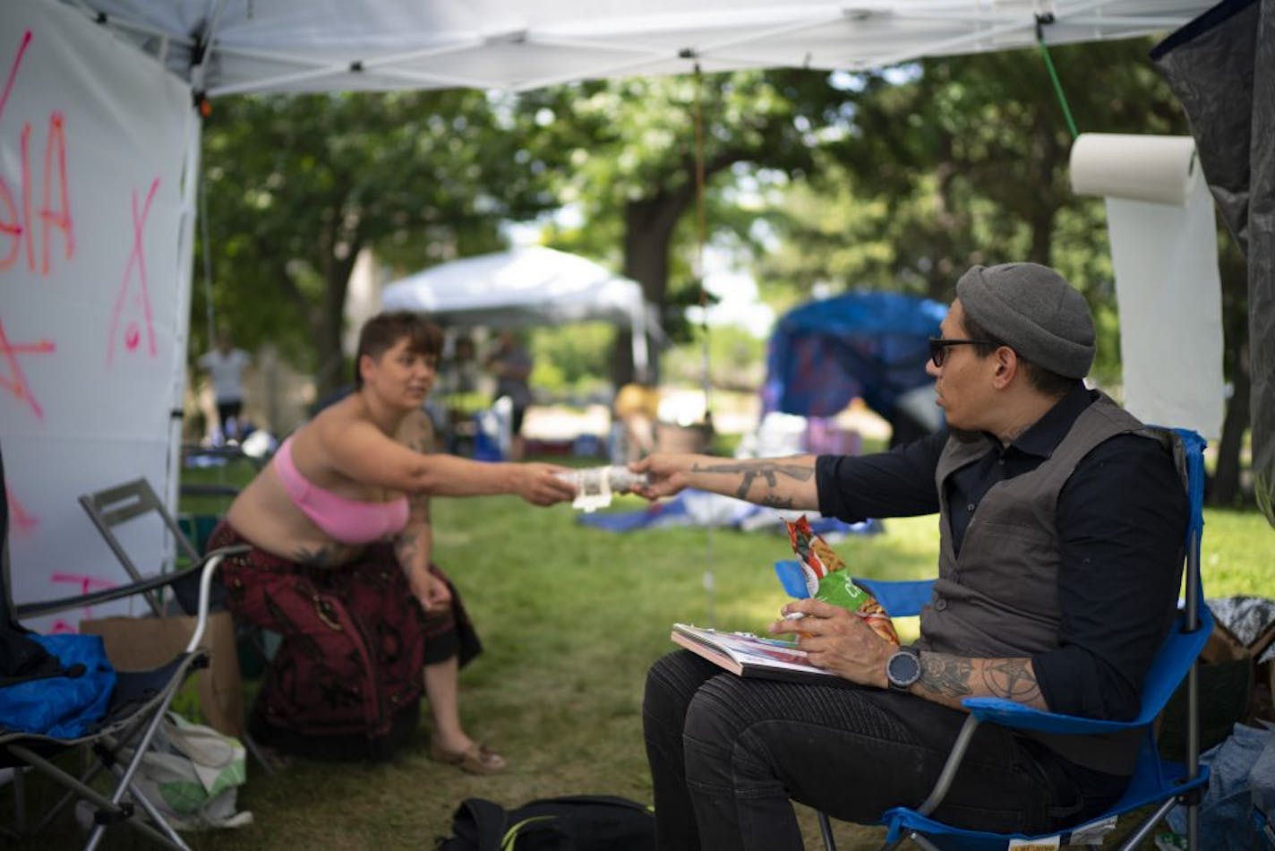 Heather Forever reached for a bundle of sage that her partner, Abraham White, was handing back to her. They were visiting while he worked on the design for a poster for an outreach organization in the shade of a tent Wednesday afternoon at Lyndale Farmstead Park.