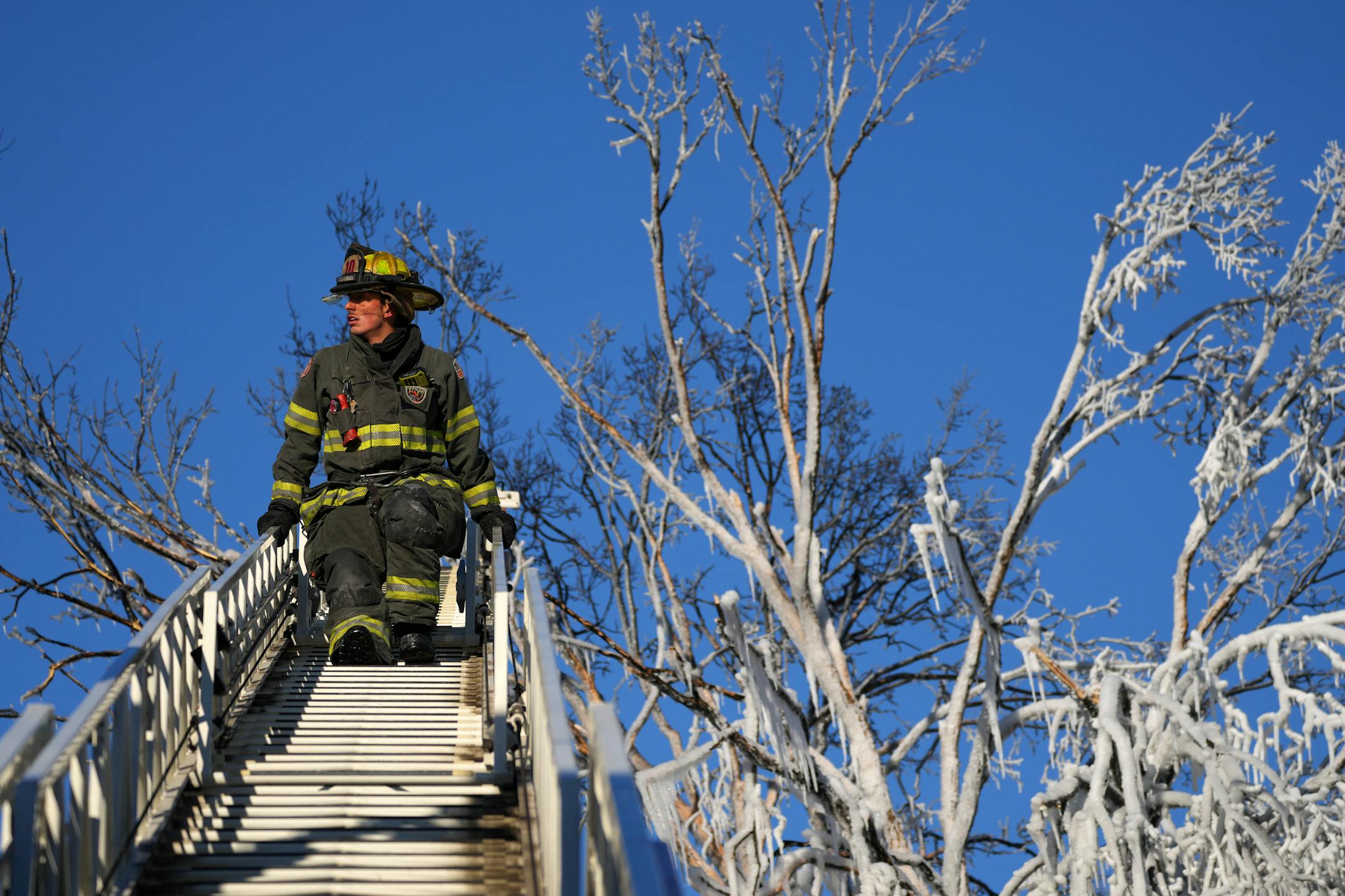 Minneapolis firefighter Toi Yamamoto works from an engine ladder to get more water on hot spots in a building fire near tree frozen from the overspray Saturday, Dec. 3, 2022 in the 2300 block of Lyndale Avenue South in Minneapolis.