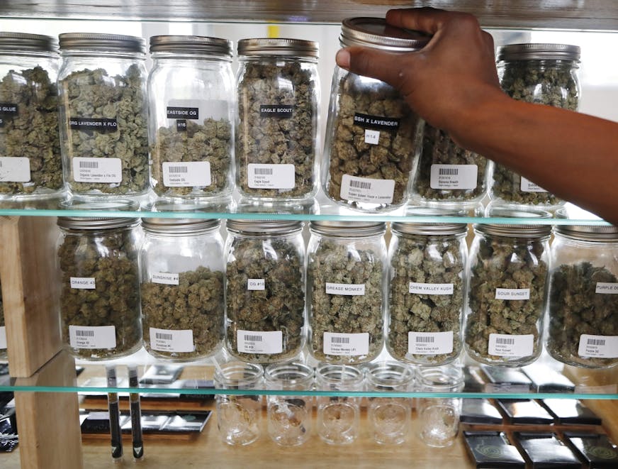 In this Tuesday, Oct. 2, 2018, photo, a clerk reaches for a container of marijuana buds for a customer at Utopia Gardens, a medical marijuana dispensary, in Detroit. Michigan and North Dakota, where voters previously authorized medical marijuana, will decide now if the drug should be legal for any adult 21 and older. They would become the 10th and 11th states to legalize so-called recreational marijuana since 2012. (AP Photo/Carlos Osorio)