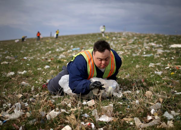 Scott Rhude, 33, sits spread-eagled in a field of garbage, reaching for a piece of trash while on a work assignment with a sheltered workshop "enclave
