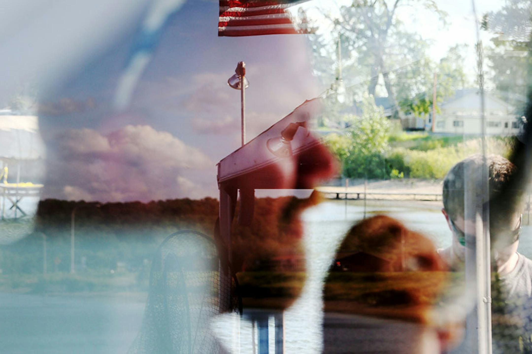 Clouds and a flag are reflected on the face of Travis Koster, the captain and fishing guide on a Twin Pines Resort boat heading out Wednesday, July 29, 2015, during an evening excursion on Lake Mille Lacs.
