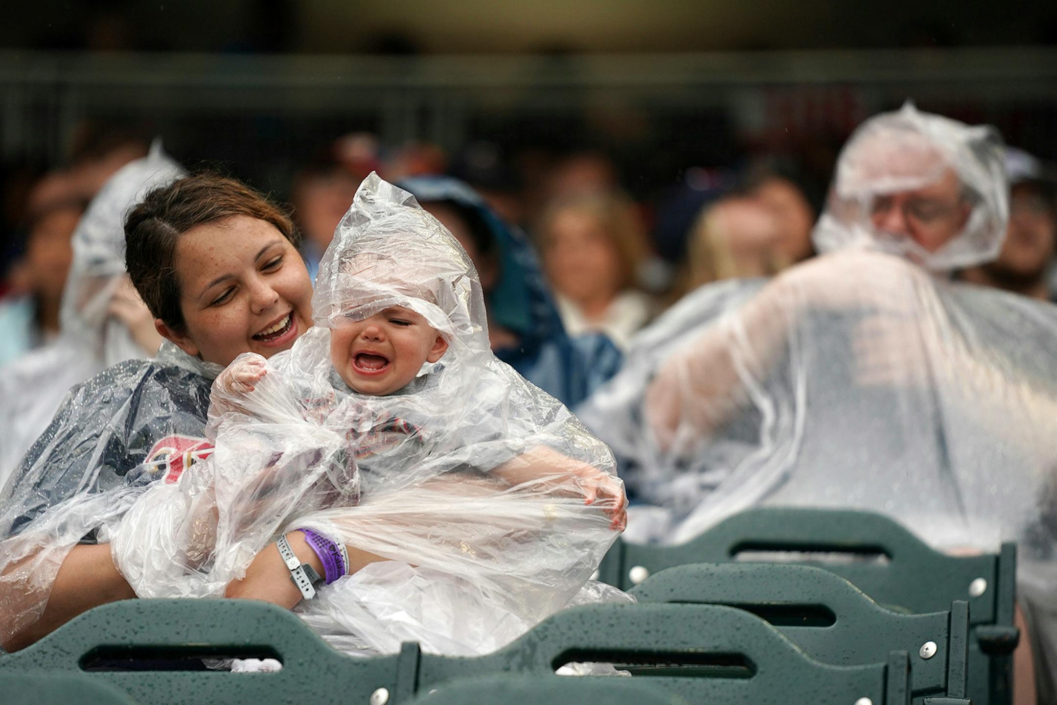 Susan Dodd of Sioux City, Iowa, tries to calm her daughter Saylor, 1, as she fought with her plastic poncho during a rain delay Friday, July 5, 2019, before a baseball game between the Texas Rangers and the Twins in Minneapolis.