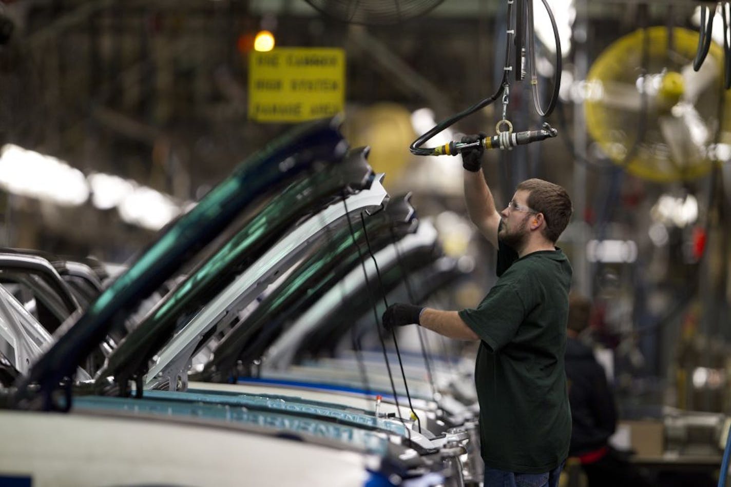 A Ford assembly line worker reached for a pneumatic wrench to install a part on the hood of a pickup truck.