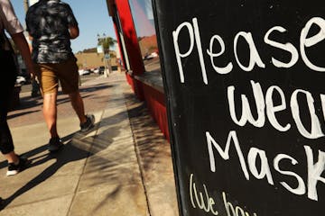 A couple walk past a sign in front of Dash of Sass clothing store along Main Street during a "Masks Up, Surf City" banner campaign to prevent coronavi