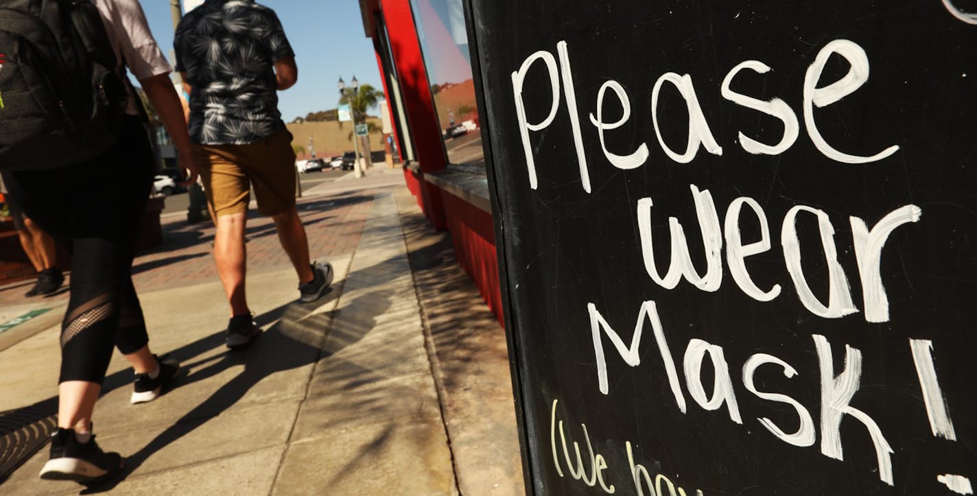 A couple walk past a sign in front of Dash of Sass clothing store along Main Street during a "Masks Up, Surf City" banner campaign to prevent coronavirus in the city of Huntington Beach, California on Aug. 12, 2020. (Genaro Molina/Los Angeles Times/TNS) ORG XMIT: 1765001