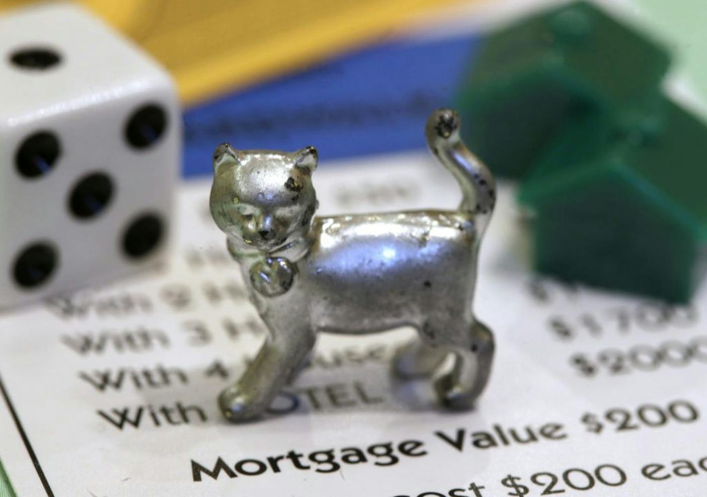 The newest Monopoly token, a cat, rests on a Boardwalk deed next to a die and houses at Hasbro Inc. headquarters, in Pawtucket, R.I., Tuesday, Feb. 5, 2013. Voting on Facebook determined that the cat would replace the iron token.