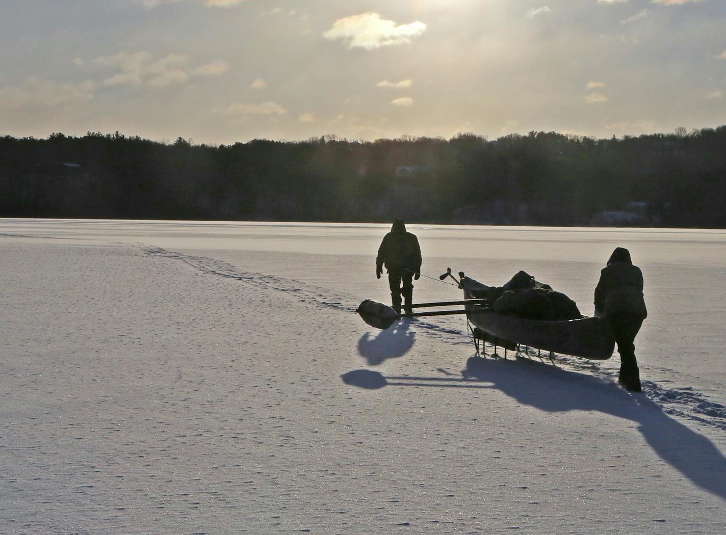 Wearing waders cinched at the waist, and also wearing life jacketes, Wendell and Galina Diller tentatively make their way across thin ice. When they reach open water, or break through, they will climb into the canoe and paddle. The outrigger provides stability while getting into the canoe.