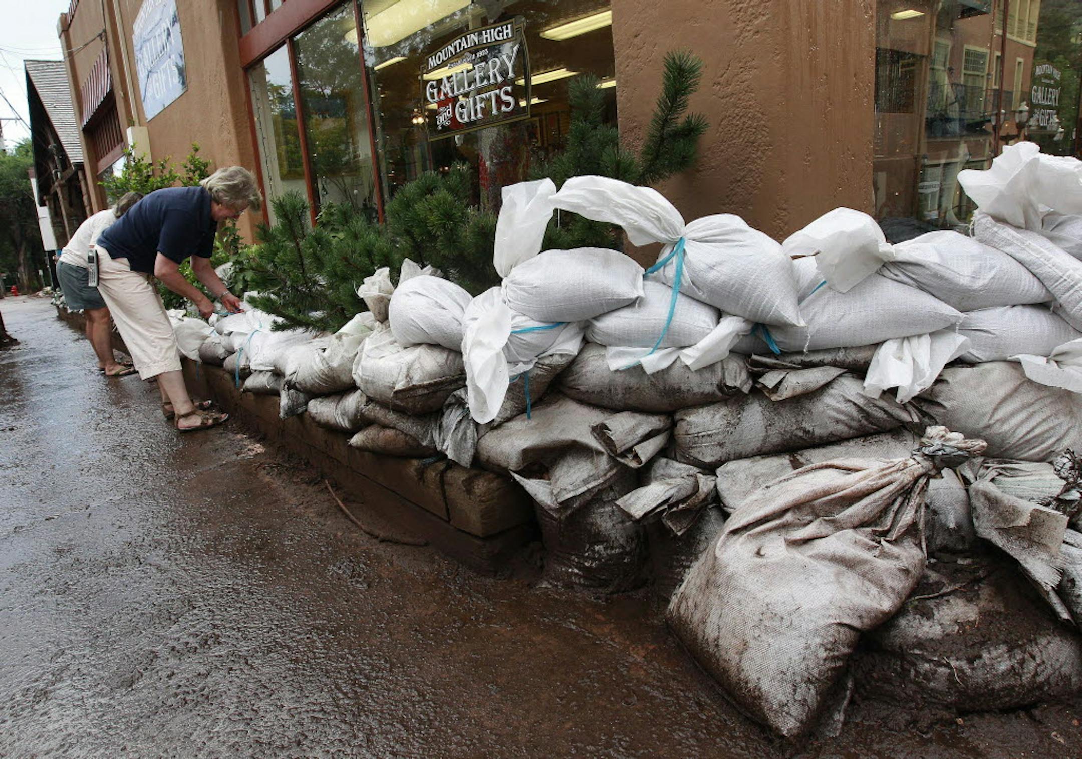 Women sandbag a shop days after a flash flood struck Manitou Springs, Colo., Monday.