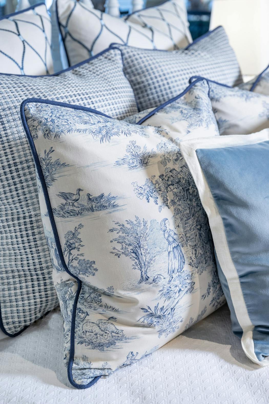 The pillows on this bedscape mix blue and white toile with similarly colored woven, embroidered, and velvet fabrics. 