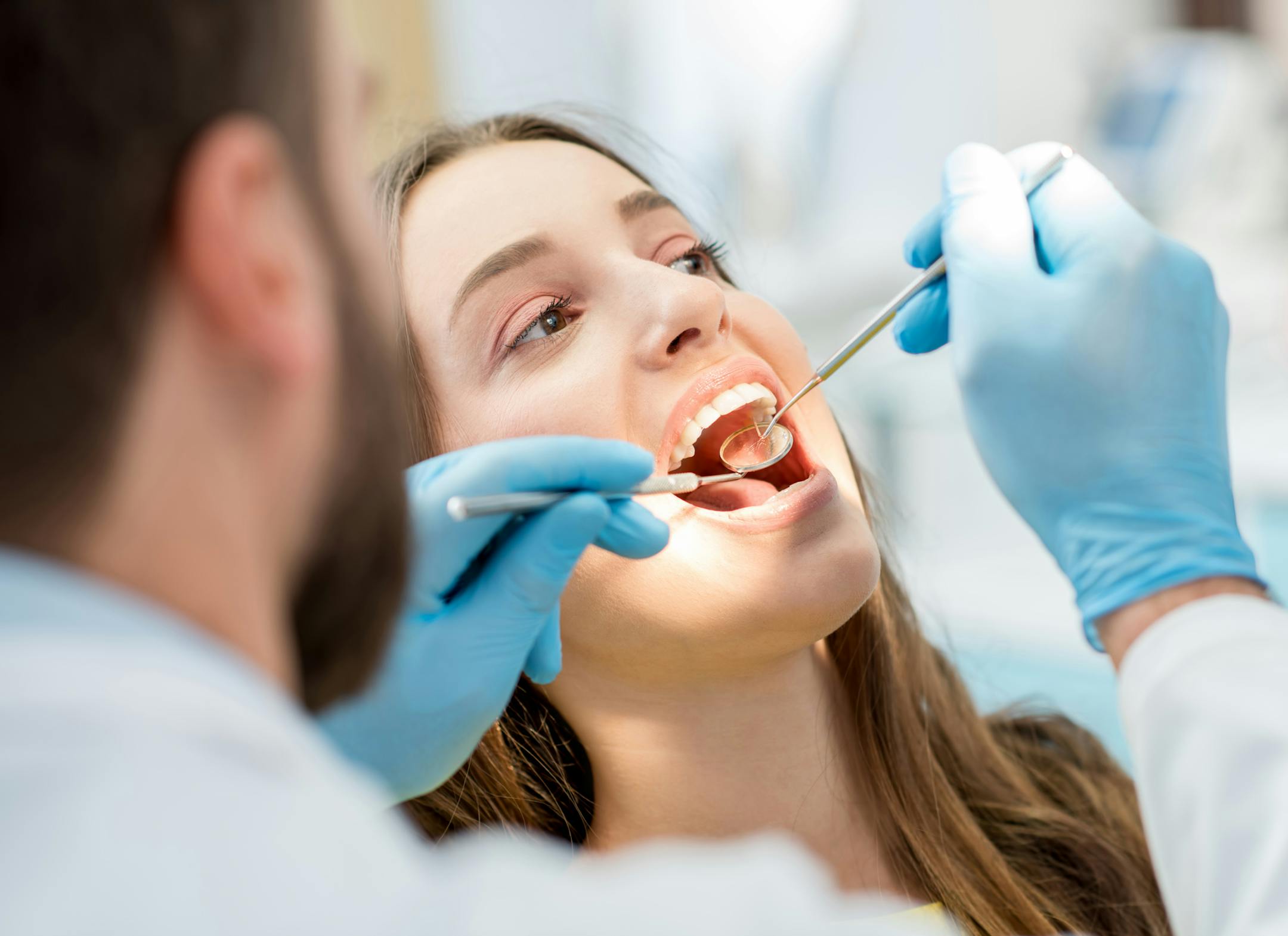 Dentist examining patient teeth with a mouth mirror and dental excavator. Close-up view on the woman's face