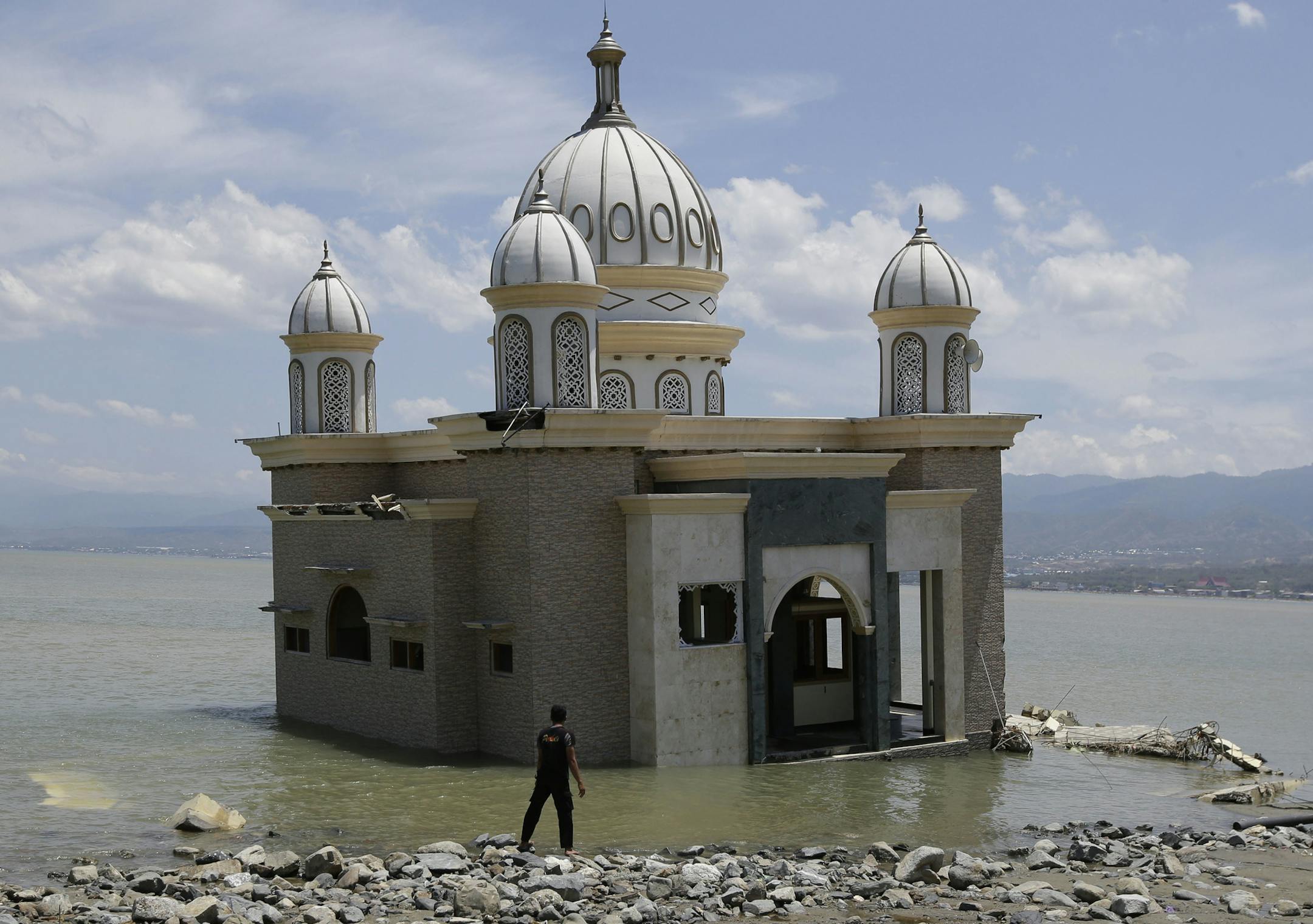 A man looks at a mosque that is isolated by water after its bridge was broken due to the massive earthquake and tsunami in Palu, Central Sulawesi, Indonesia Friday, Oct. 5, 2018. French rescuers say they've been unable to find the possible sign of life they detected a day earlier under the rubble of a hotel that collapsed in the earthquake a week ago on Indonesia's Sulawesi island. (AP Photo/Aaron Favila) ORG XMIT: XAF124