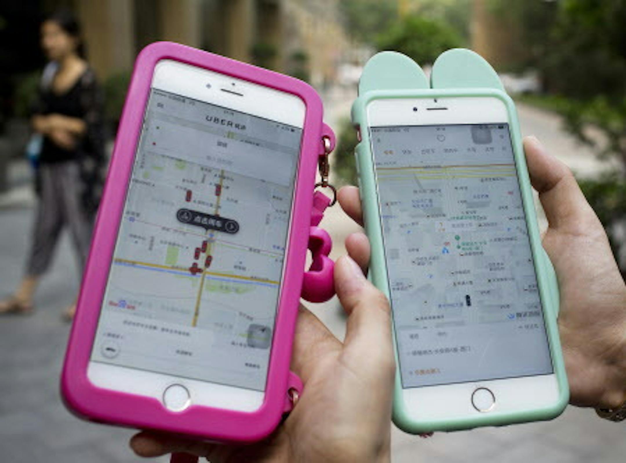 Women holding their smartphones show the ride-hailing apps Uber Technology Ltd., left, and Didi Chuxing at a residential compound in Beijing, Monday, Aug. 1, 2016. Uber Technology's main Chinese rival, Didi Chuxing, says it is acquiring the U.S. ride-hailing service's China operations, linking the companies in a business alliance after a costly battle for market share. Monday's announcement marked a surrender by another foreign technology brand to intense competition in China. (AP Photo/Andy Won
