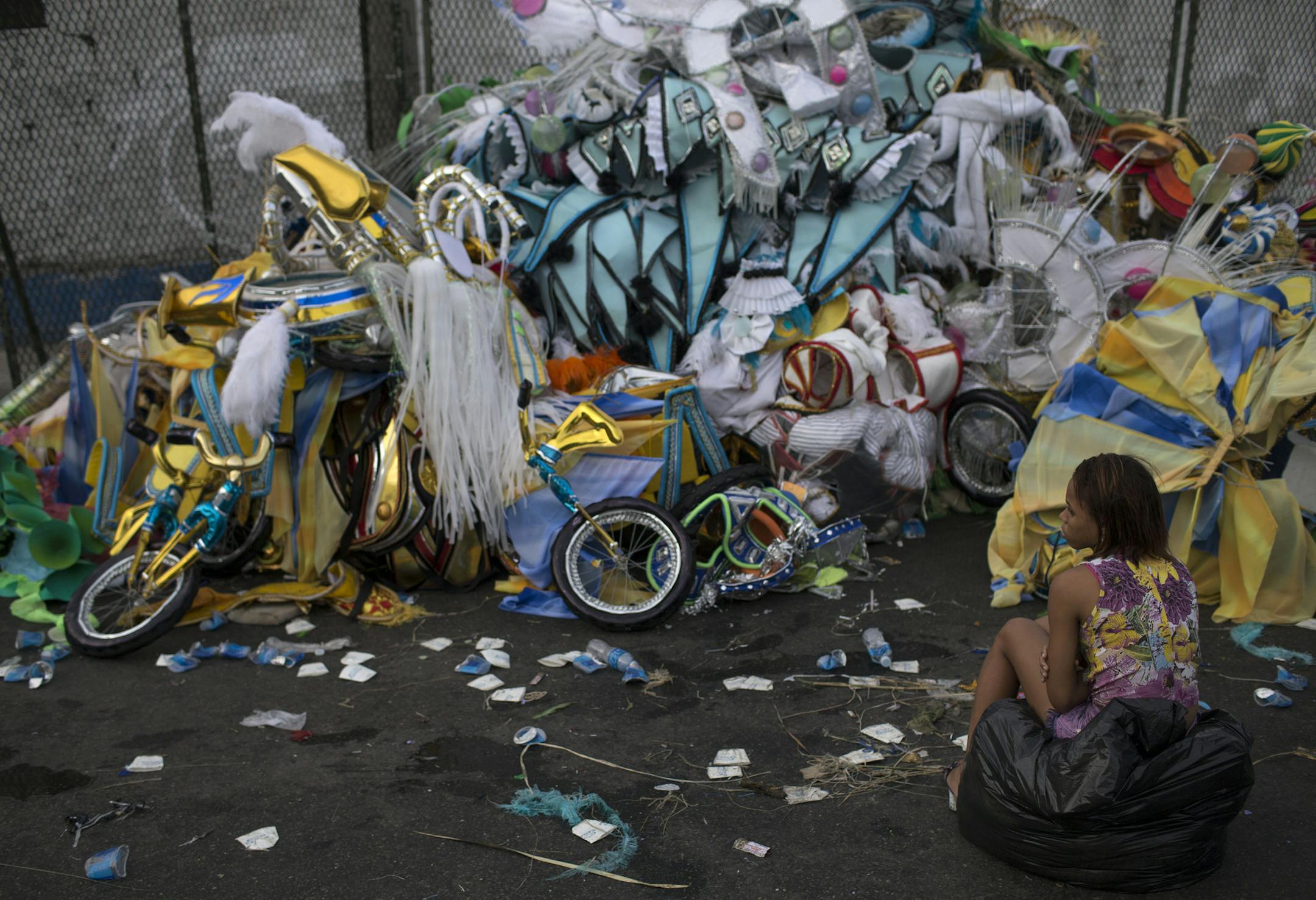 A woman sits in front of a pile of discarded carnival costumes after carnival celebrations at the Sambadrome in Rio de Janeiro, Brazil, Tuesday, March 4, 2014. The costumes on display at the all-night parade that ended early Tuesday have made RioÌs Carnival celebration the most famous in the world. But the handmade confections often have a short shelf life. As the tens of thousands of revelers stream out of the Sambadrome, a surprising number of them immediately abandon their costumes. (AP