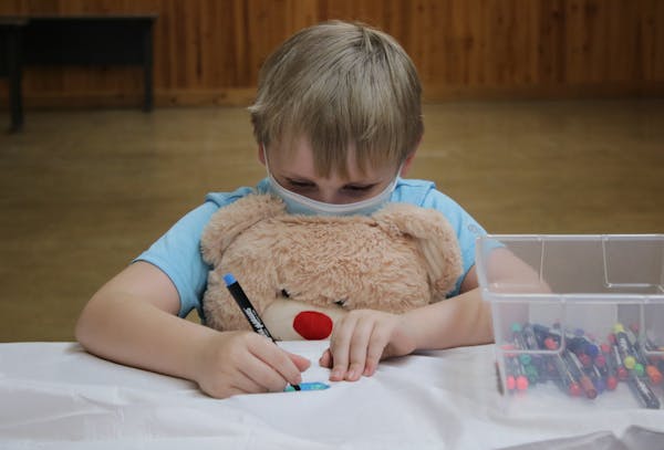 A young participant drew a picture, supported by an oversized teddy bear. The camp, run by nonprofit Children's Grief Connection, was founded nearly 2