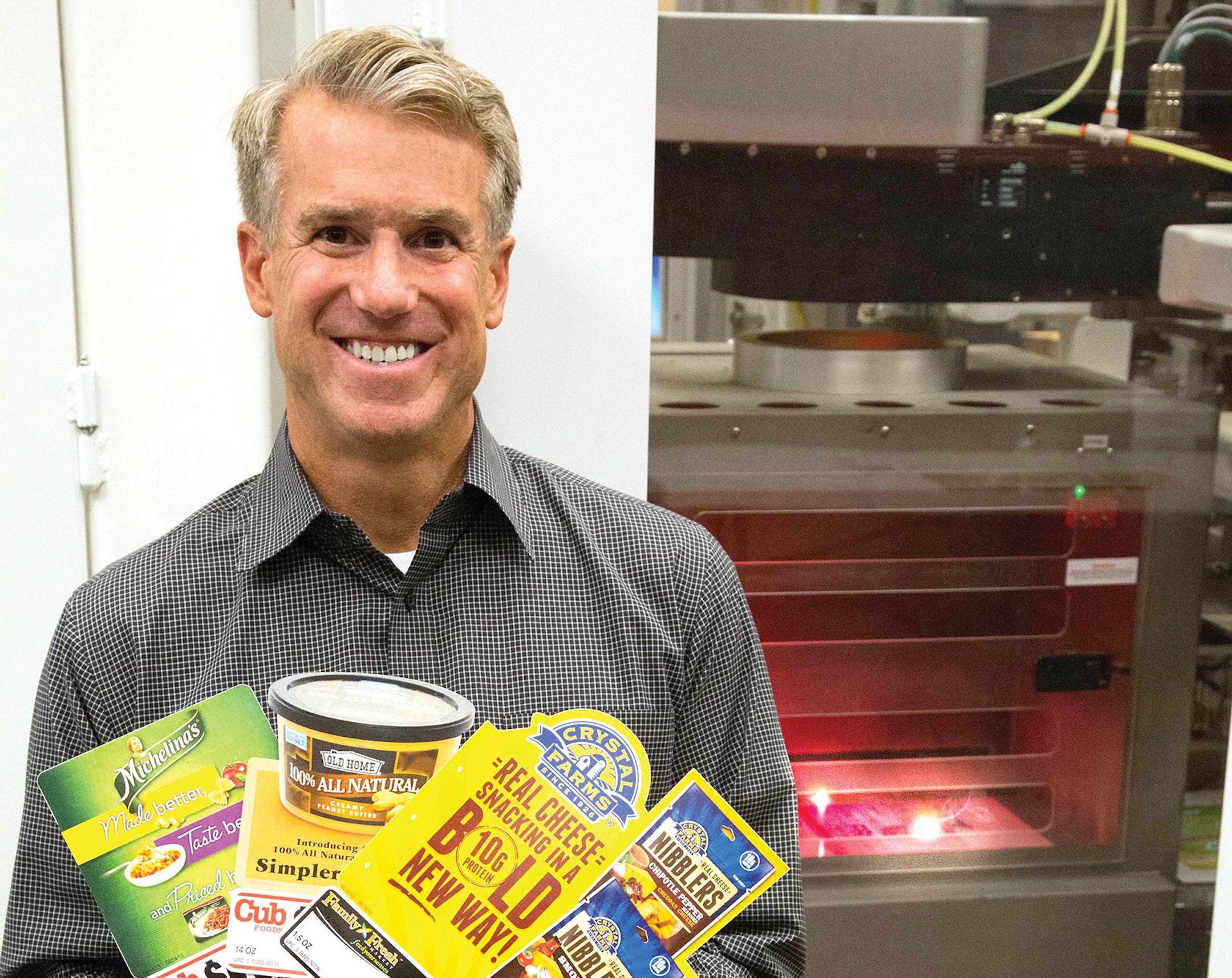 CEO Glen Dall of Insignia Systems shows several in-store point-of-purchase signs the company makes for consumer-food companies on its new laser die-cut production system for more than 22,000 retailers. Source: Insignia Systems
