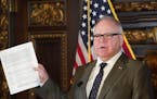 Gov. Tim Walz held up a supplemental budget at a news conference in 2020.
