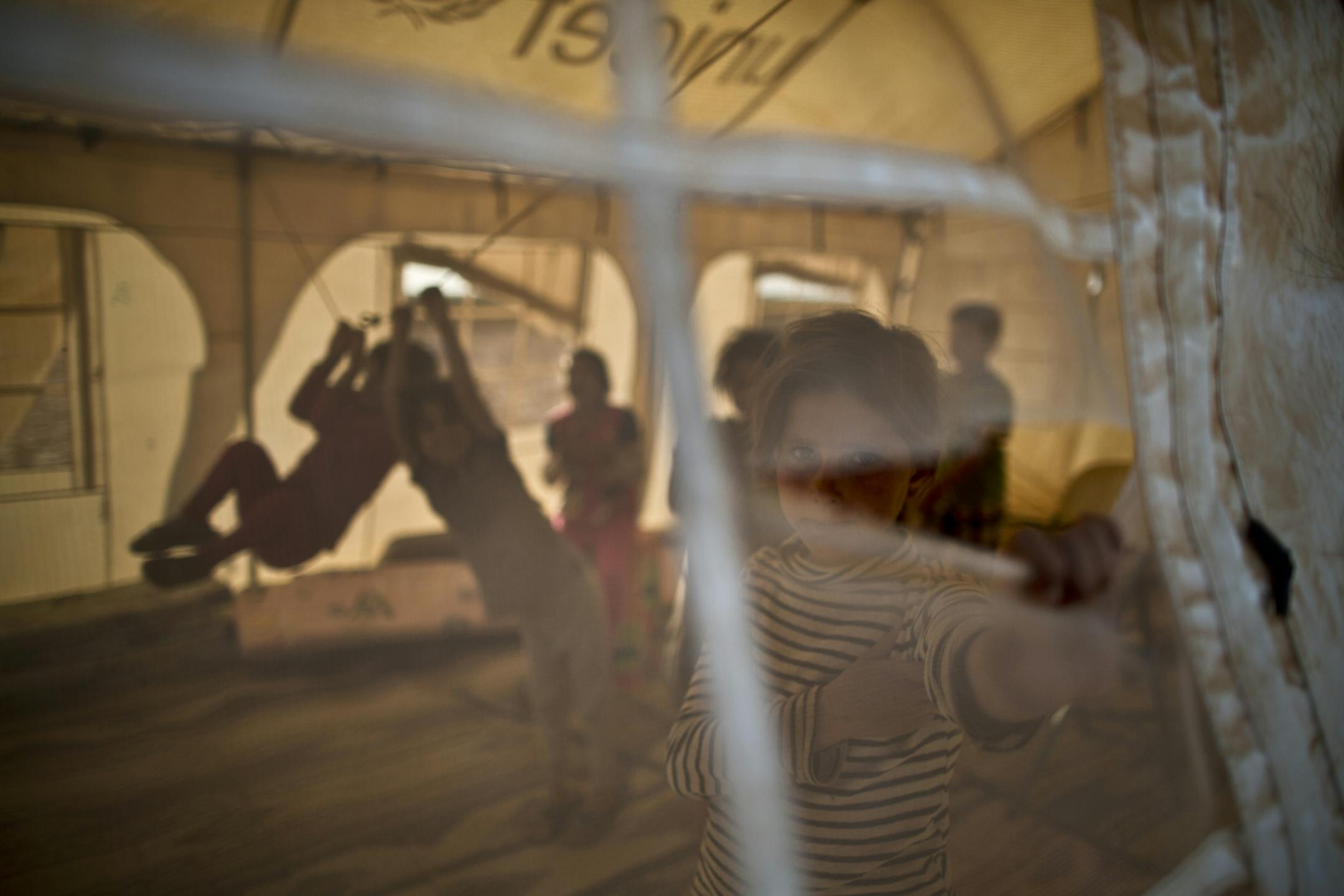 In this Wednesday, July 22, 2015 photo, a Syrian refugee girl looks through the hole of a makeshift school at an informal tented settlement near the Syrian border on the outskirts of Mafraq, Jordan. More than 10,000 children have died in Syria's four-year conflict, while over 2.8 million in and out of the country don�t go to school, according to the U.N. children's agency, UNICEF.