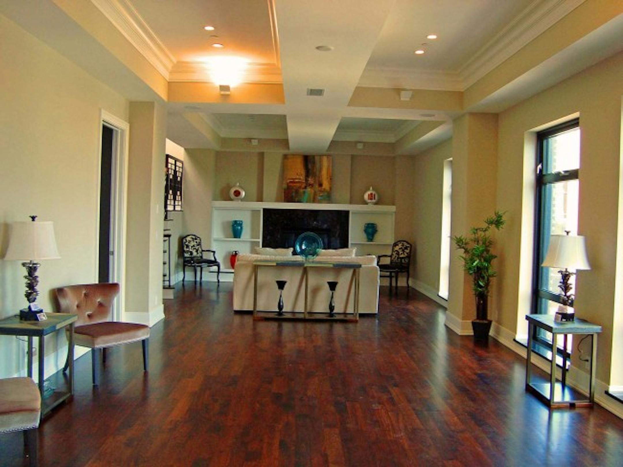 The main-floor living room features multiple tray ceilings, rich walnut floors and ample windows.