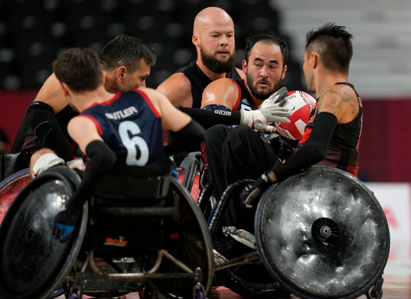 Charles Aoki of the United States, second right holds the ball under pressure from Zak Madell of Canada, rear, during a Wheelchair Rugby pool phase group match at the Tokyo 2020 Paralympic Games, Thursday, Aug. 26, 2021, in Tokyo, Japan. (AP Photo/Shuji Kajiyama)