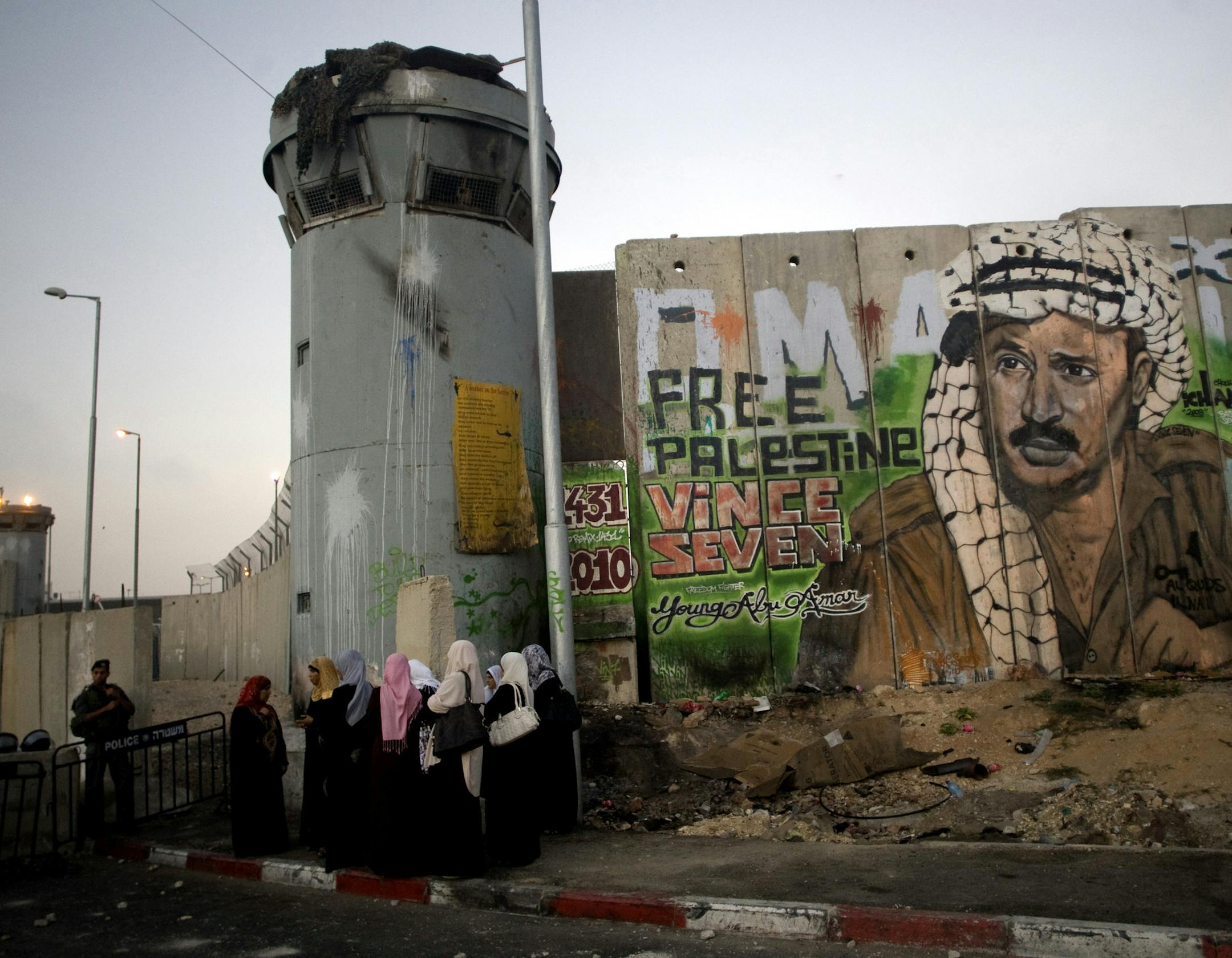 File - In this Friday, Aug. 13, 2010 file photo, Palestinian women wait near a section of Israel's separation barrier covered in graffiti, one depicting the late Palestinian leader Yasser Arafat, at the Qalandiya checkpoint , between Jerusalem and the West Bank city of Ramallah. Israel began construction of its 150-mile (250-kilometer) separation barrier in 2002 in response to a wave of Palestinian suicide bombings. Israel says the structure is a defense measure. But because it frequently juts i