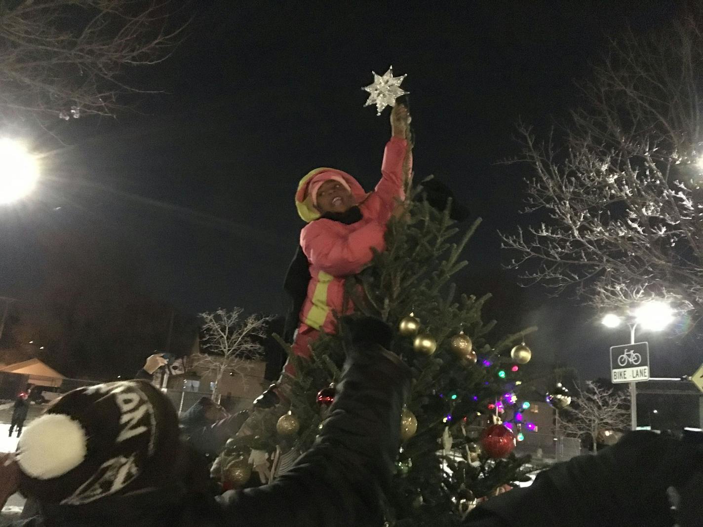 Blessing Caldwell, a first grader from North Minneapolis, gets a boost as she places the star atop the community Christmas tree outside the Fourth Police Precinct. The new tree was a neighborhood response to one in the precinct that officers had decorated with cigarette carton, fast food wrappers and a cup from a fried chicken restaurant.