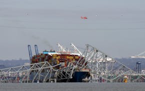 A helicopter flies over a container ship as it rests against wreckage of the Francis Scott Key Bridge on Tuesday, as seen from Pasadena, Md.