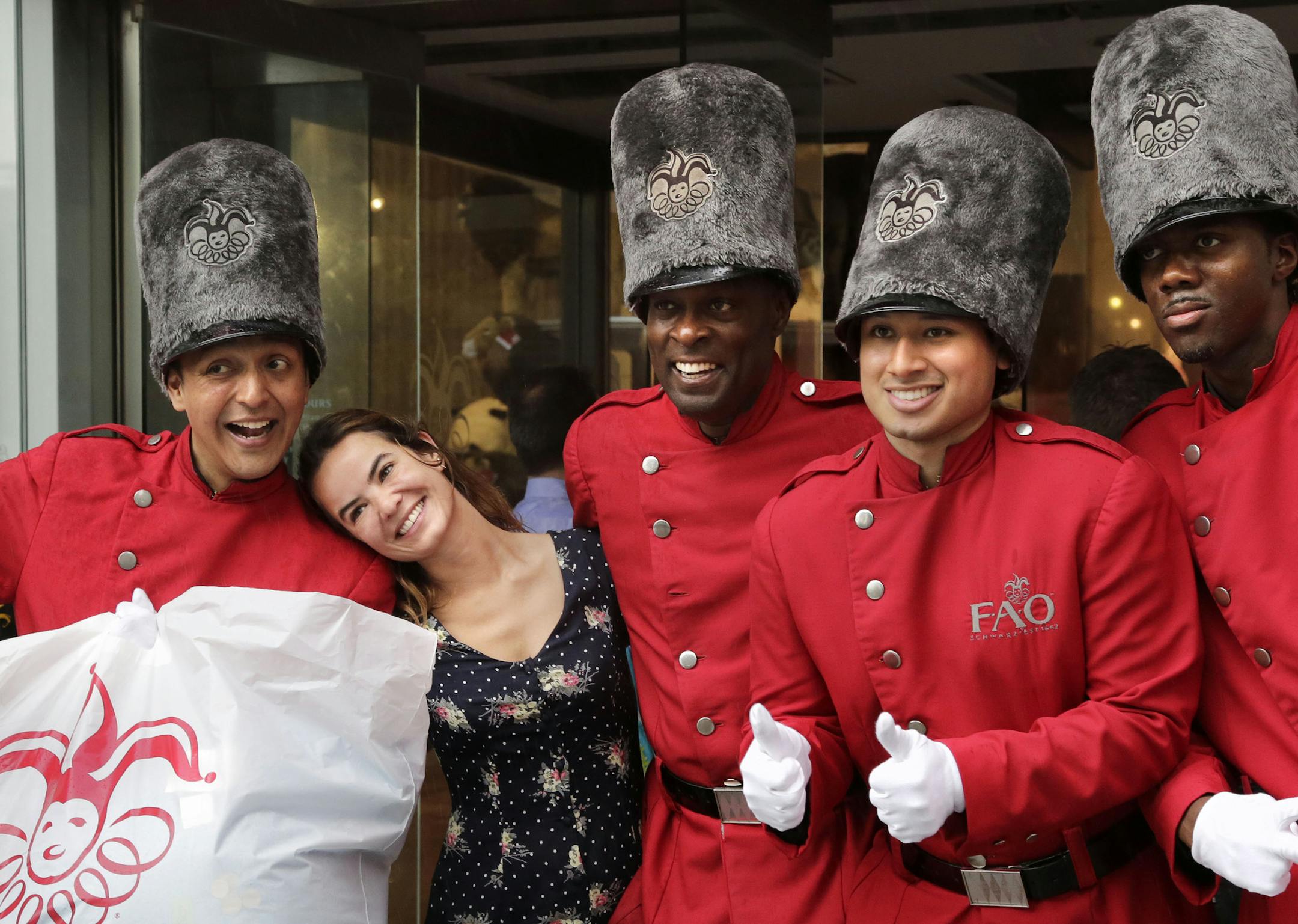 Ana Assuncao, of Rio de Janeiro, Brazil, second left, poses for photos with four "toy soldiers" in front of the flagship FAO Schwarz toy store on Fifth Avenue in New York, Wednesday, July 15, 2015. The store, probably the best-known toy store in the world, is closing Wednesday night. (AP Photo/Mark Lennihan)