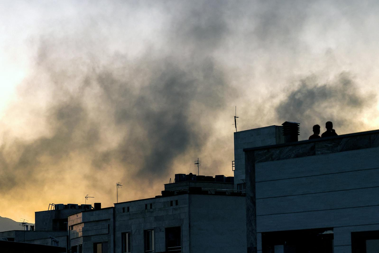 People stand on a rooftop amidst billowing smoke following an overnight Israeli strike in Tehran, Iran, on June 17, 2025.  
