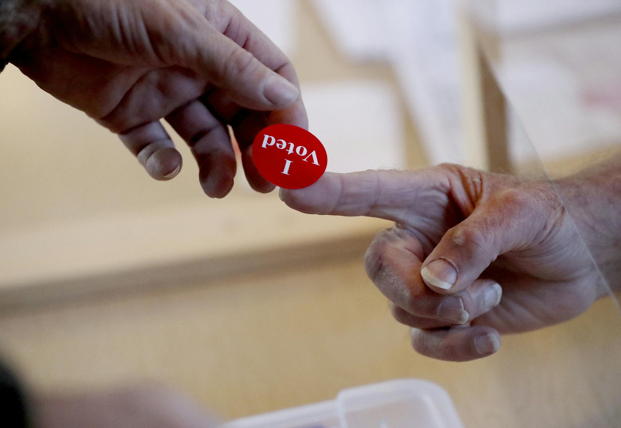 Al Lindell, head election judge, hands a voting sticker to a voter from behind a plexiglass barrier as voters casts their ballots on Election Day, Tuesday, Nov. 3, 2020, at the Vasa Town Hall in Welch, Minn. (David Joles/Star Tribune via AP)