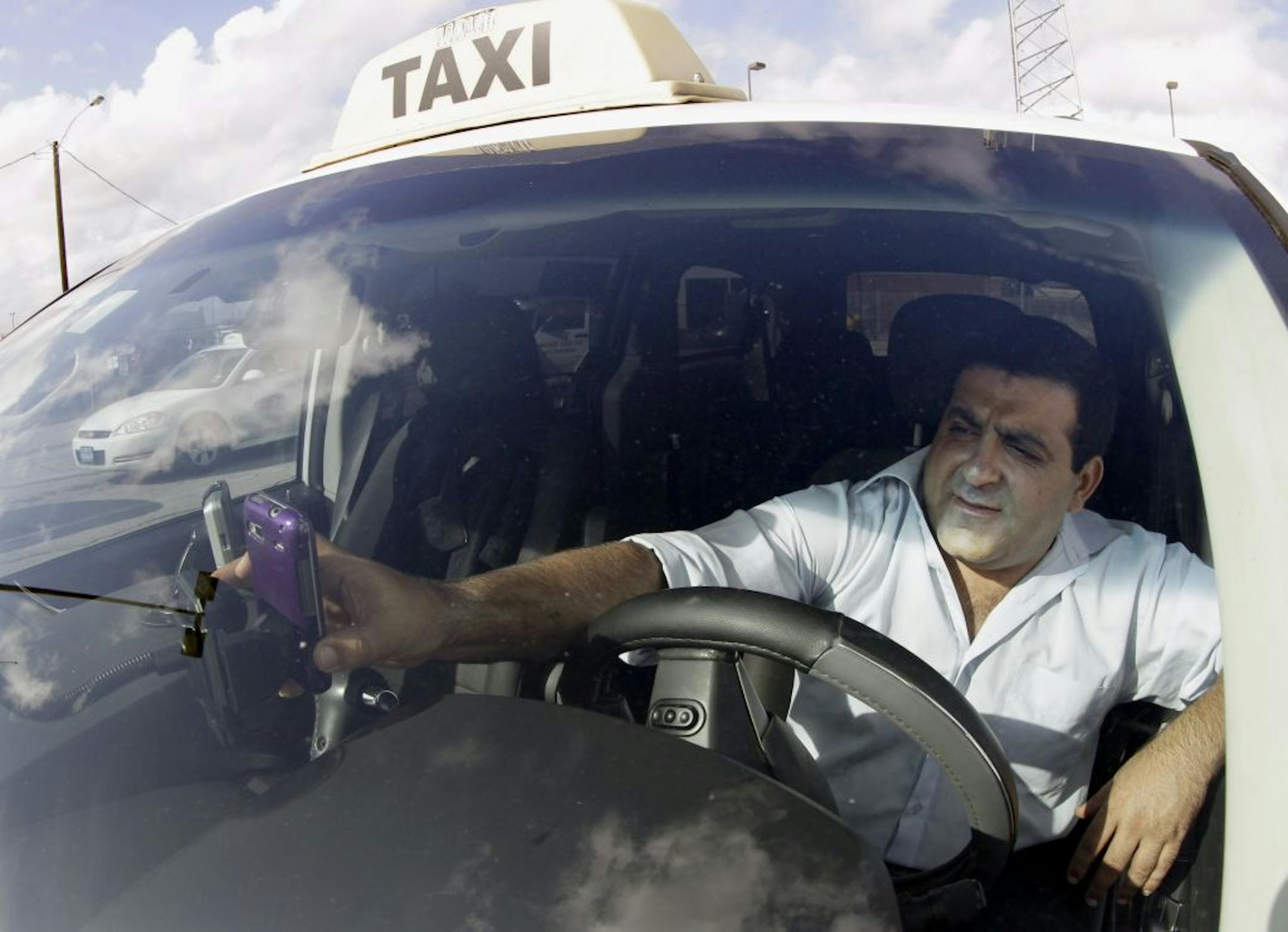 Independent taxi driver Matthew Bahar places his cellphone back in a cradle inside his taxi while waiting to pickup customers at Hobby Airport Wednesday, Dec. 14, 2011, in Houston.