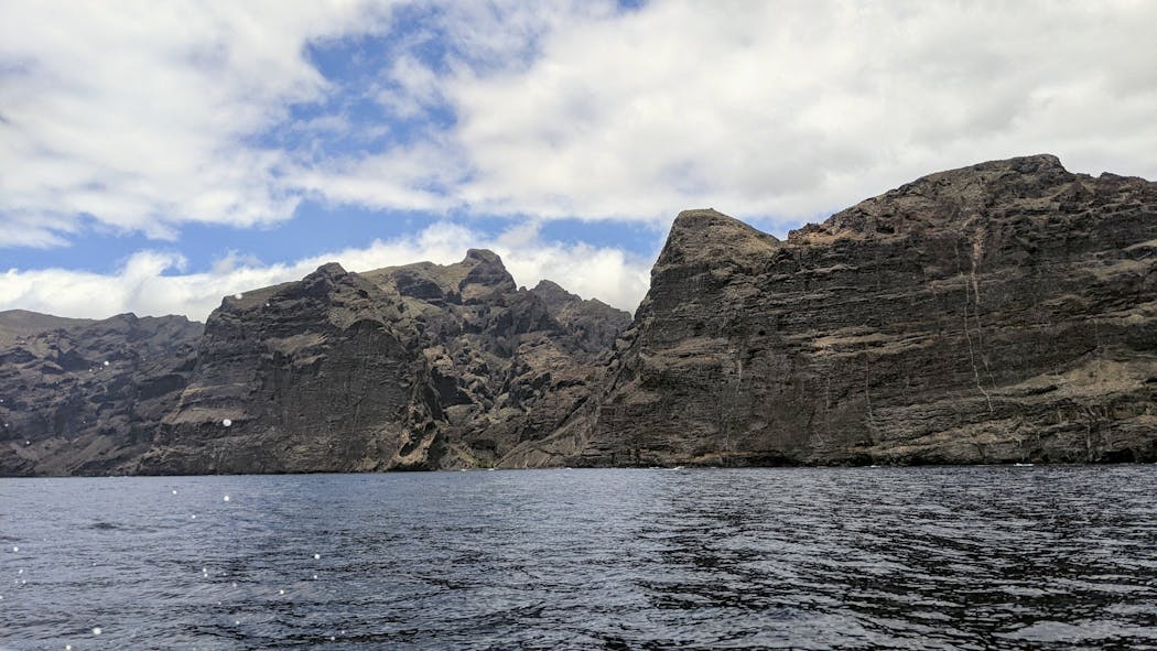 A tour boat approaches the bay of Masca, overlooking the soaring cliffs of Los Gigantes on Tenerife in the Canary Islands.
