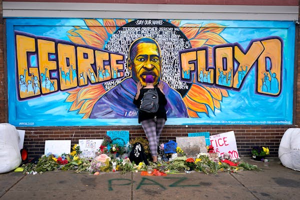FILE - Damarra Atkins pays respect to George Floyd at a mural at George Floyd Square in Minneapolis, April 23, 2021. Minneapolis will buy the boarded-