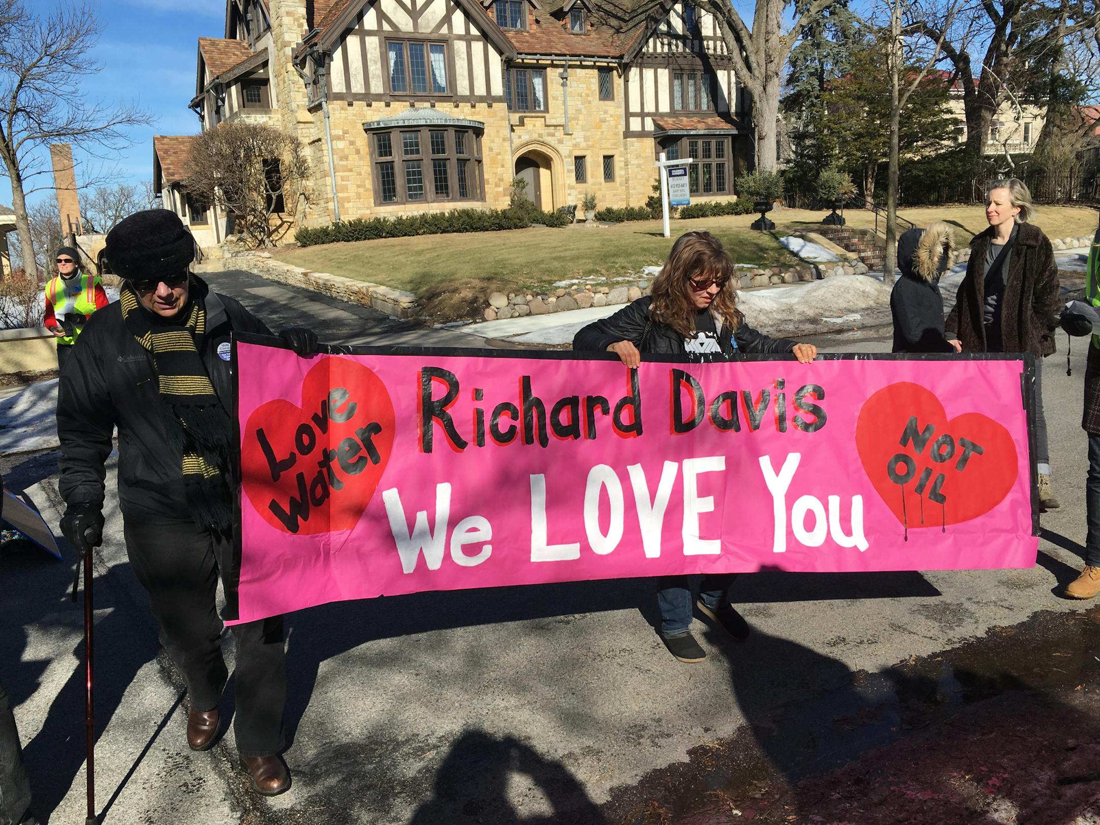 Marchers gathered outside the home of Richard Davis, CEO of US Bank hold a banner.