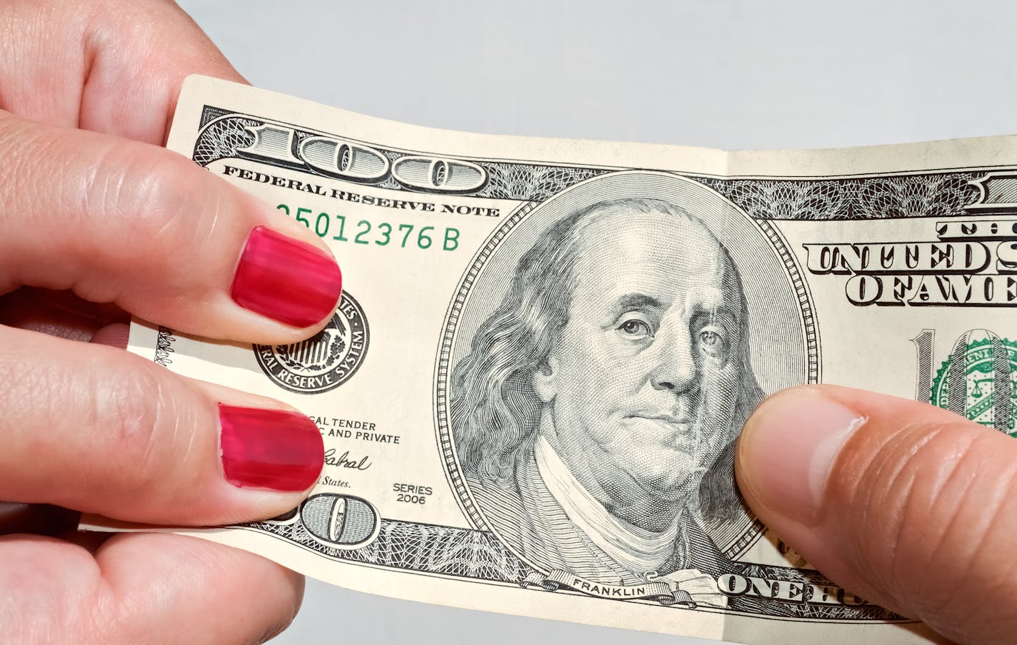 Closeup of hands pulling a hundred dollar banknote