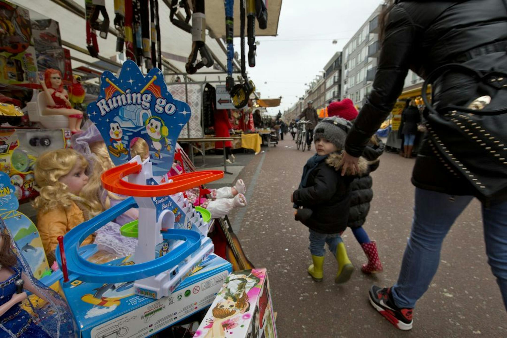 This March 20, 2013 photo shows a mother urging her children away from toys in a stand at Albert Cuyp market, Amsterdam, Netherlands. Amsterdam's wealth began in its port with the merchants who bought and sold everything from tulip bulbs to spices from the East Indies. A little of that mercantile past can still be seen at the city's many markets. The most famous is the Albert Cuyp food market in the Pijp neighborhood, which sells, as the city website puts it, everything from cheese to bicycle ch