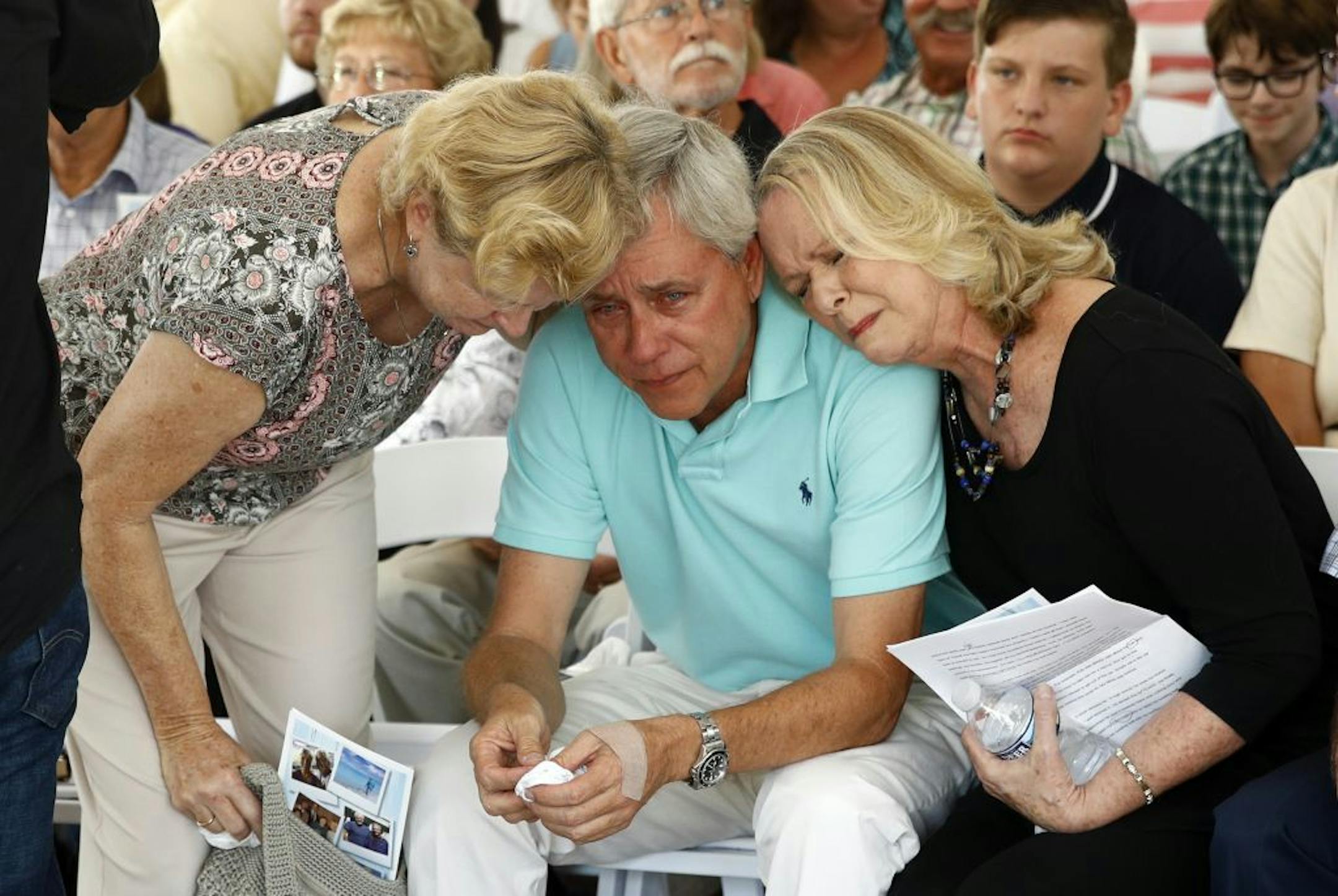 Carl Hiaasen, center, brother of Rob Hiaasen, one of the journalists killed in the shooting at The Capital Gazette newspaper offices, is consoled by his sister Judy, right, and Rob Hiaasen's widow, Maria, during a memorial service, Monday, July 2, 2018, in Owings Mills, Md.