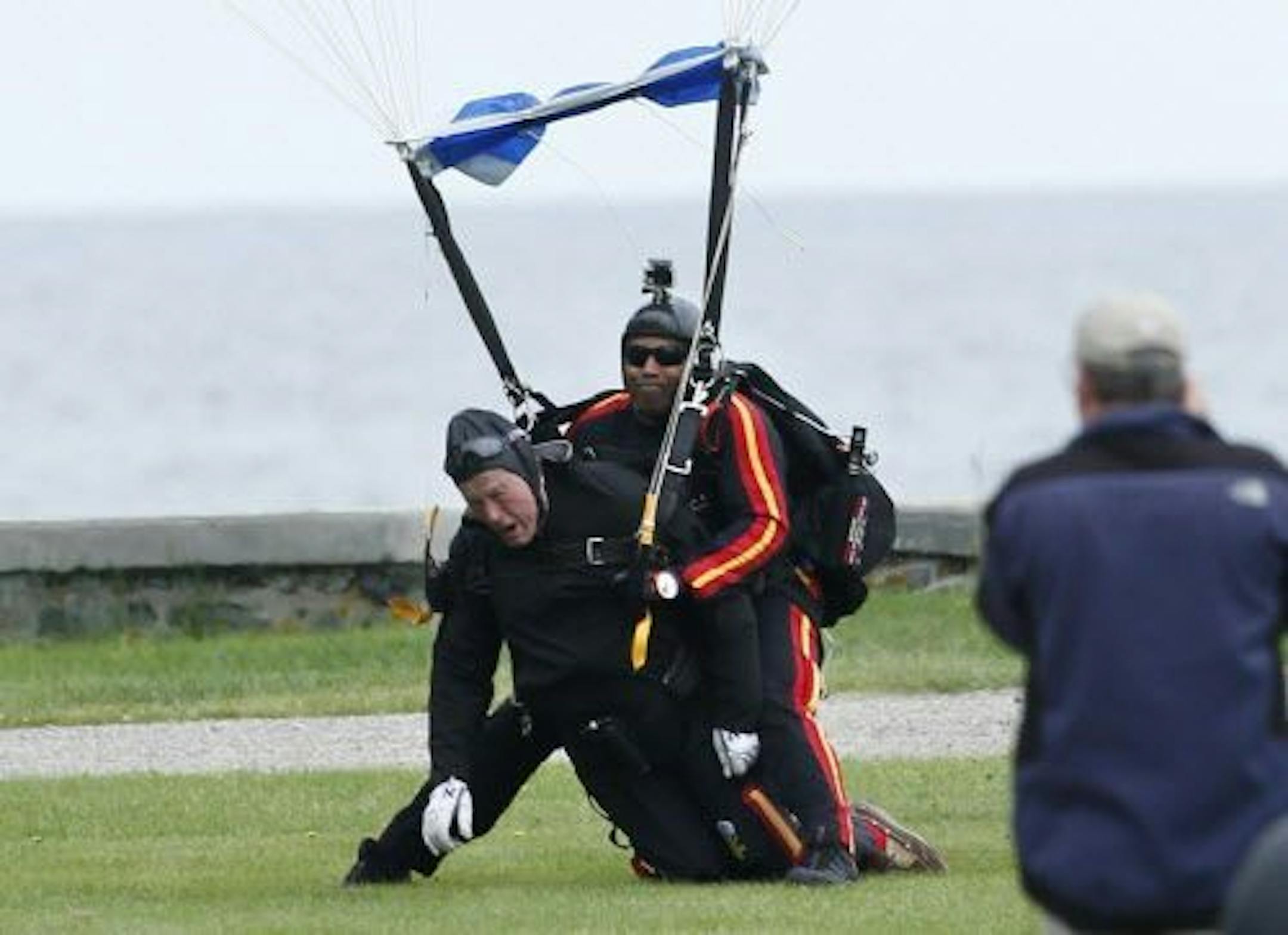 Former President George H.W. Bush, left, strapped to Sgt. 1st Class Mike Elliott, a retired member of the Army's Golden Knights parachute team, land on the lawn at St. Anne's Episcopal Church after making a tandem parachute jump near Bush's summer home in Kennebunkport, Maine, Thursday, June 12, 2014.