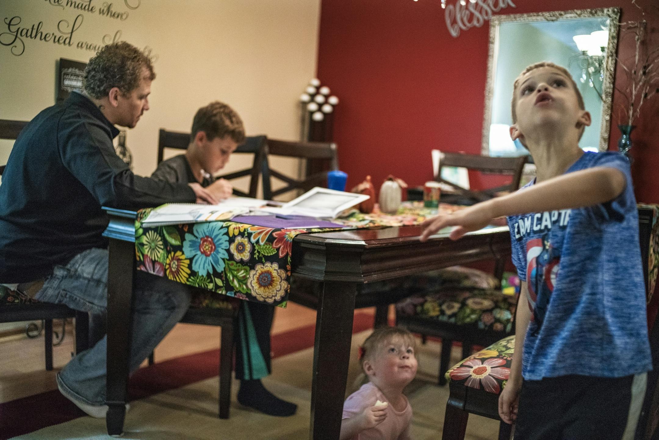 Asher,7, plays with his sister, Sabriella,2, while Alex Kempe helps oldest son Aiden,9, with his math homework.