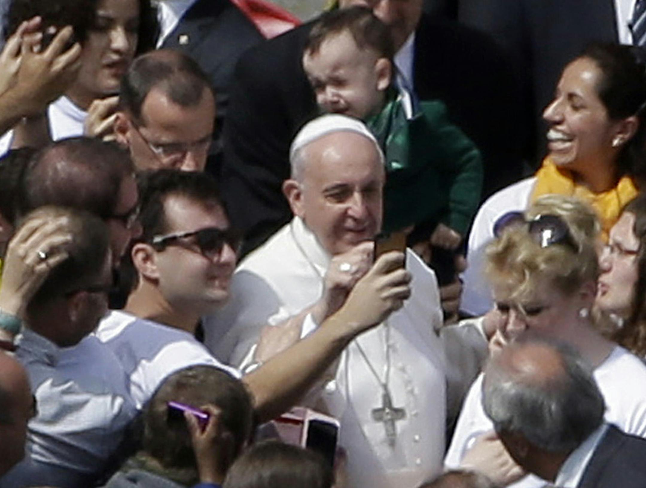 Pope Francis poses for pictures with faithful at the end of a Palm Sunday service in St. Peter's Square, at the Vatican, Sunday, April 13, 2014. Pope Francis, marking Palm Sunday in a packed St. Peter's Square, ignored his prepared homily and spoke entirely off-the-cuff in a remarkable departure from practice. Later, he hopped off his popemobile to pose for "selfies" with young people in the crowd. In his homily, Francis called on people, himself included, to look into their own hearts to see ho