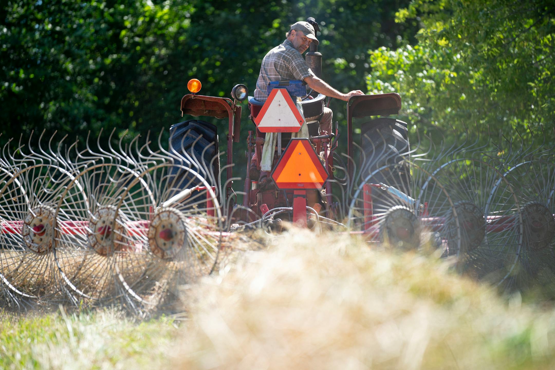 Max Gustafson rakes hay with his tractor Thursday, July 21, 2022 on rented land near his farm in Center City.
