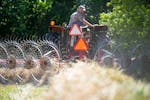 Max Gustafson rakes hay with his tractor Thursday, July 21, 2022 on rented land near his farm in Center City.