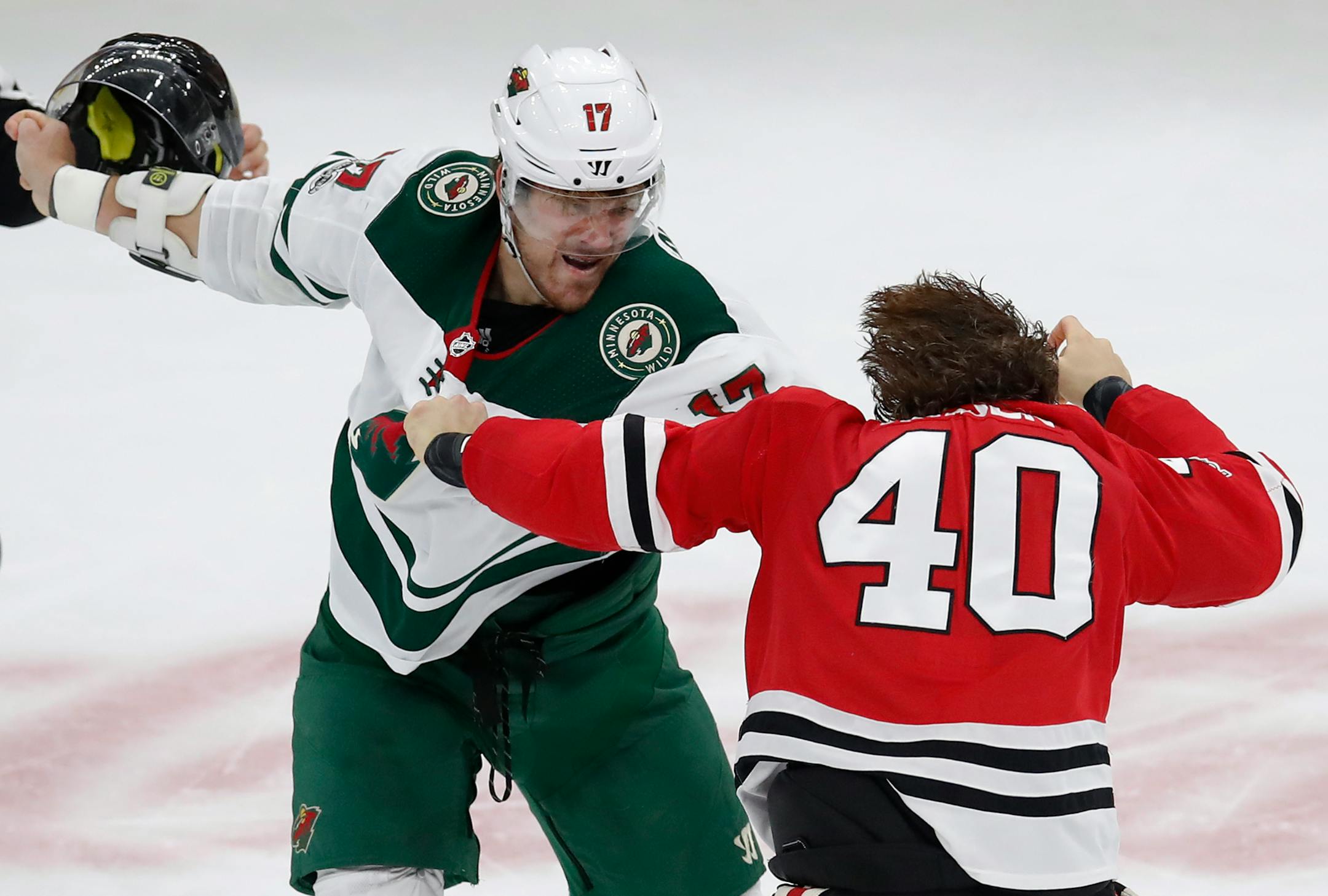Minnesota Wild's Marcus Foligno, left, holds the helmet of Chicago Blackhawks' John Hayden during a fight in the second period of an NHL hockey game Thursday, Oct. 12, 2017, in Chicago. (AP Photo/Jim Young)