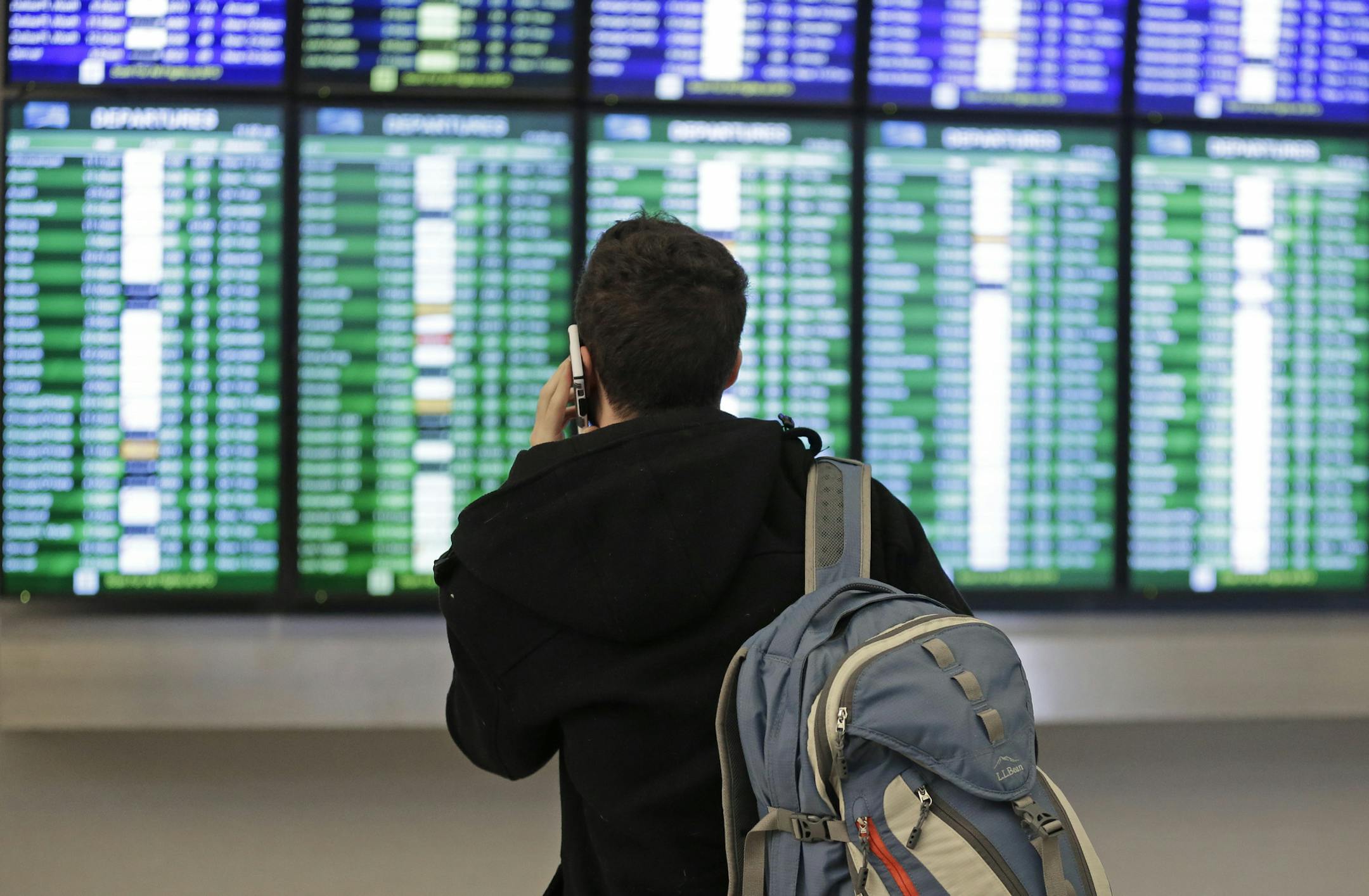 FILE - In this Friday, Jan. 22, 2016, file photo, a traveler speaks on the phone as he views the arrival and departure board at San Francisco International Airport in San Francisco. U.S. airlines have canceled several thousand flights through Tuesday, March 14, 2017, as a winter storm heads toward the Northeast. The major airlines are waiving ticket-change fees that range up to $200 for customers who want to change their travel plans. Restrictions vary by airline. (AP Photo/Ben Margot, File)